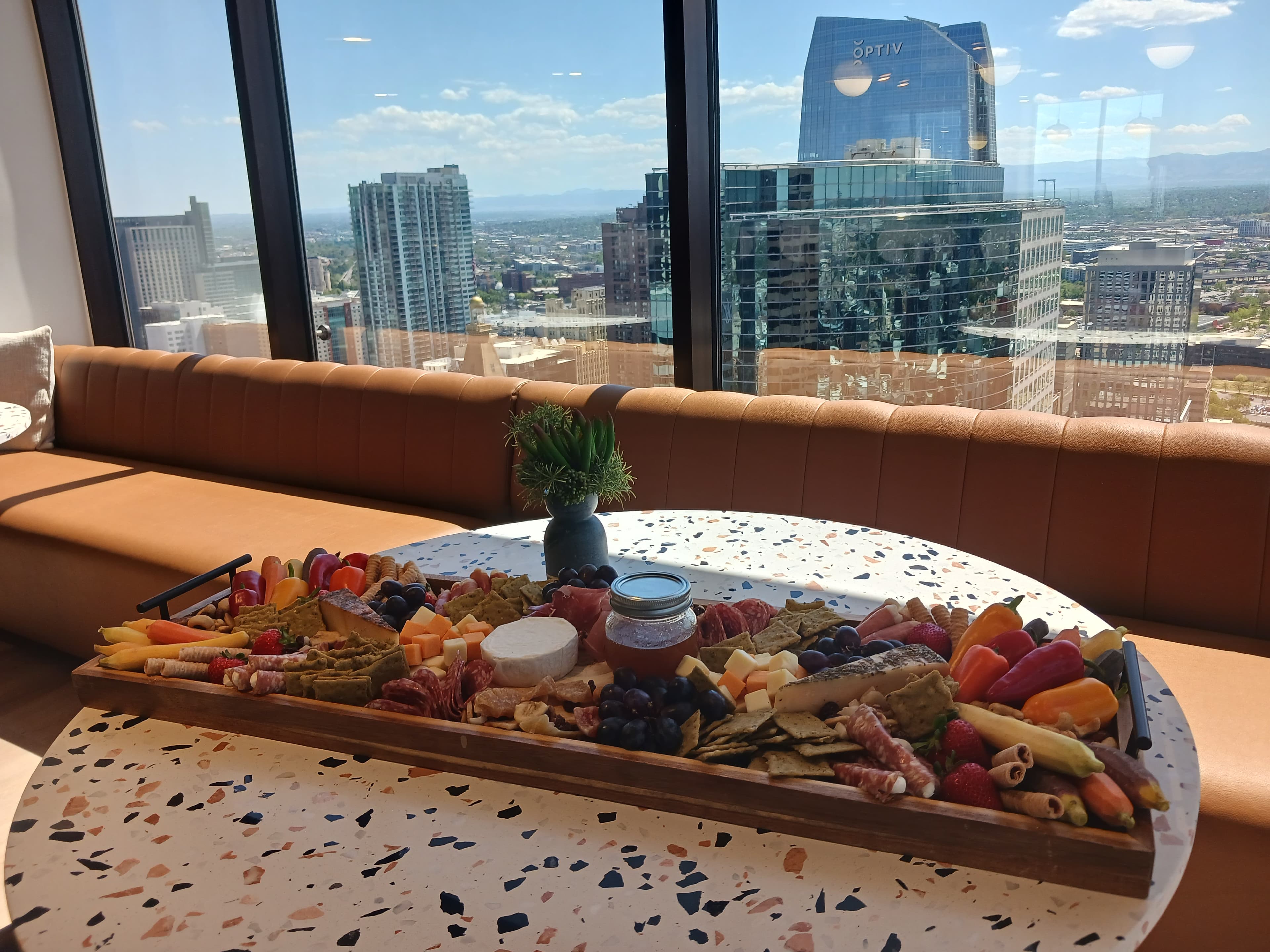 Grazing board with charcuterie, cheeses, fruit, and veggies set against a Denver skyline