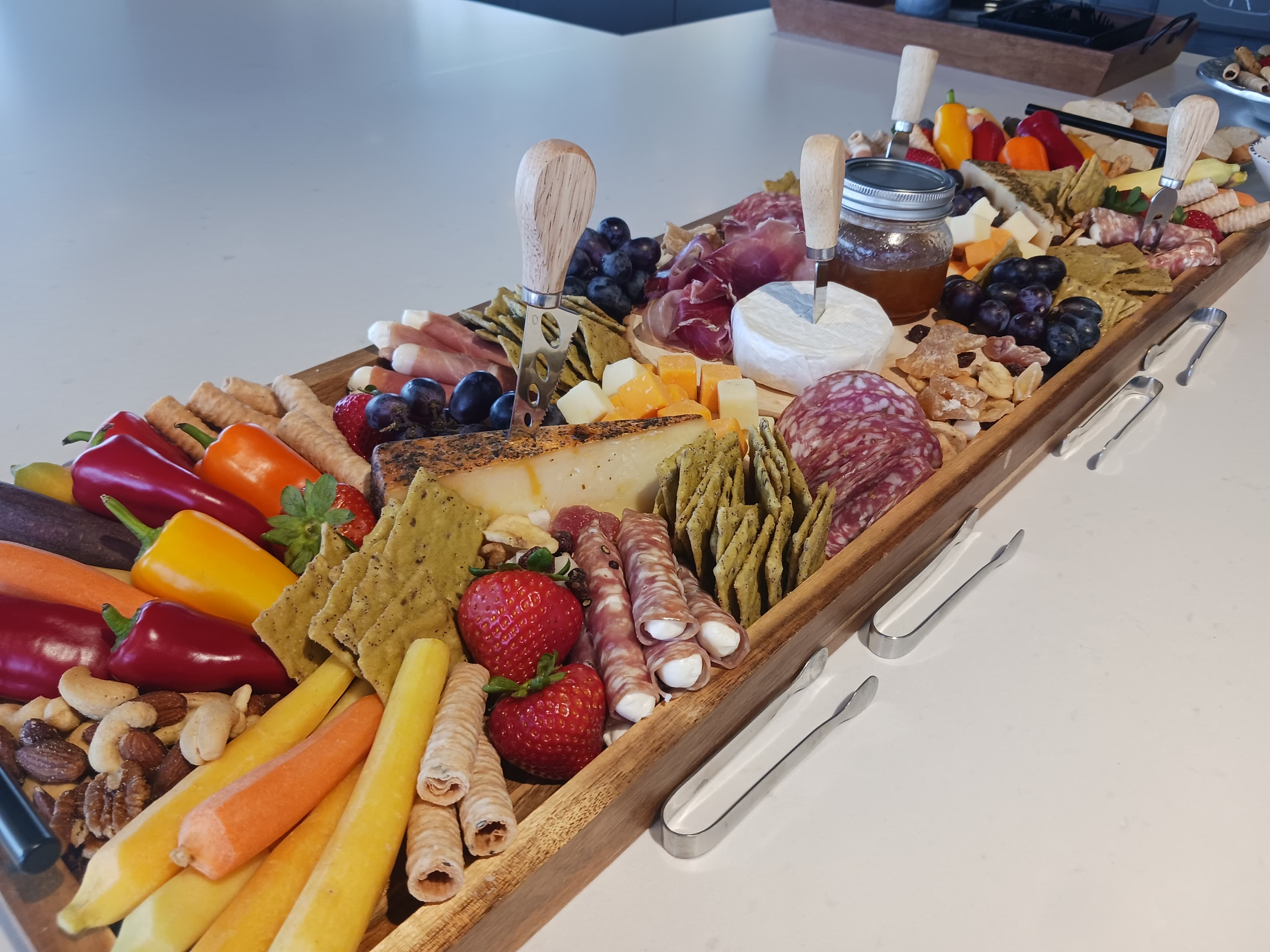 Overflowing grazing board with crudité, charcuterie, strawberries, nuts, and cheeses